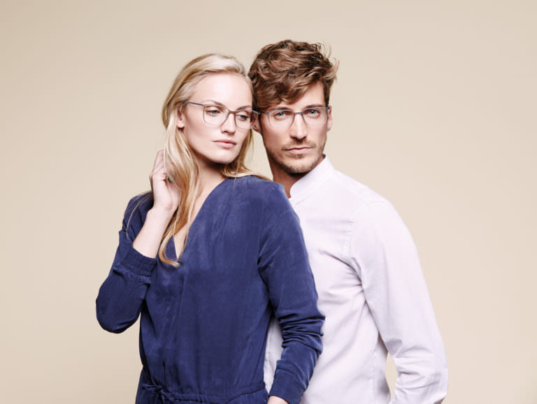 Woman wearing Silhouette Urban Lite 2886 plastic eyeglass frames in tan/silver with man wearing Silhouette Urban Lite 2884 plastic eyeglass frames in smoke gray/navy.
