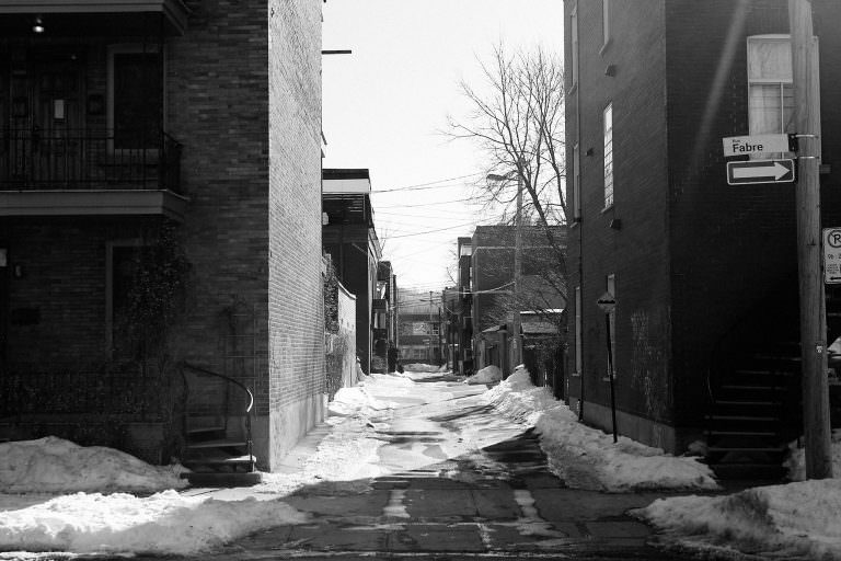 A desolate street with snow piles in an older urban neighbourhood.